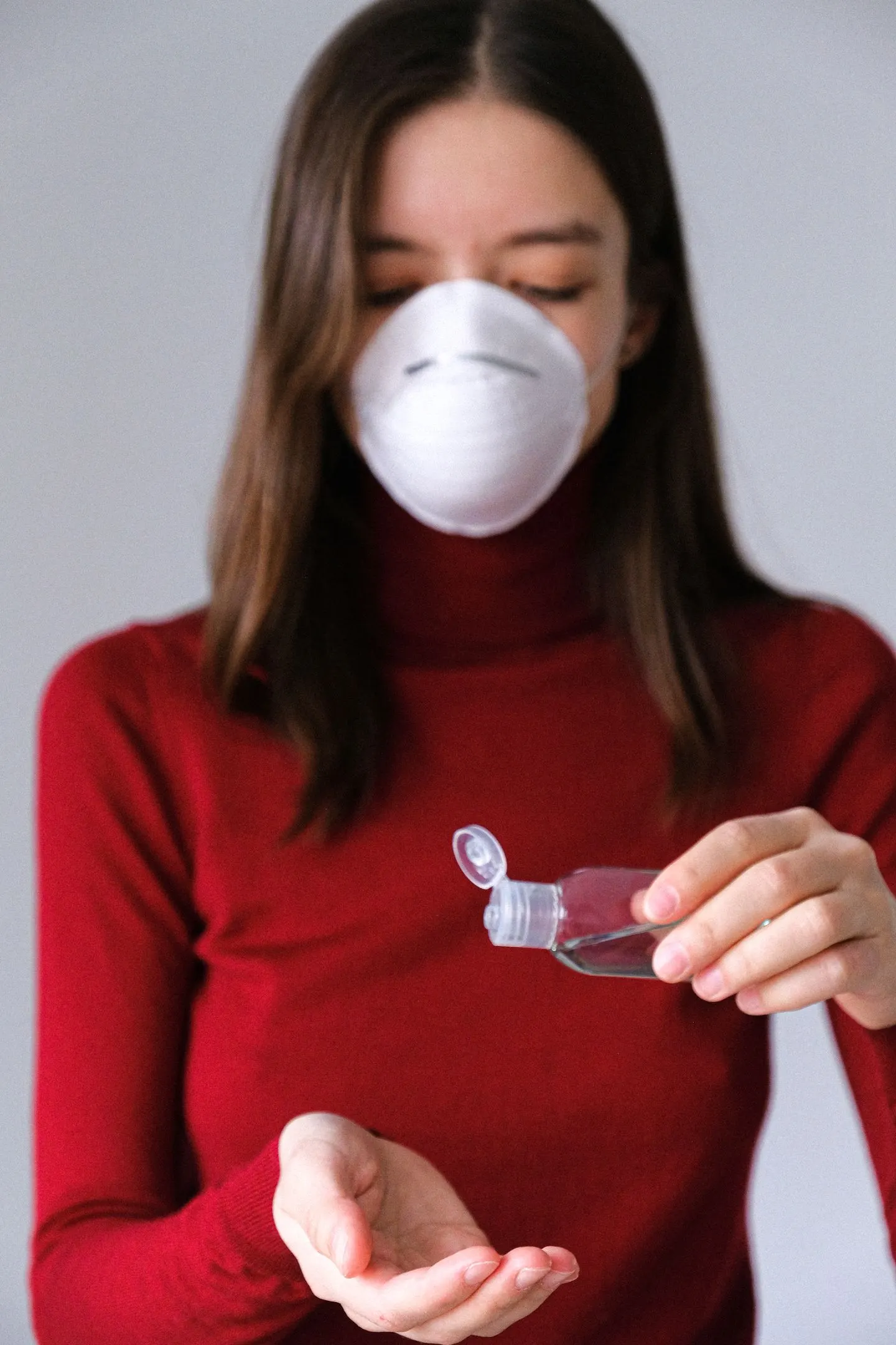 Frau mit Maske gießt Flüssigkeit aus einer kleinen Flasche in ihre Hand.